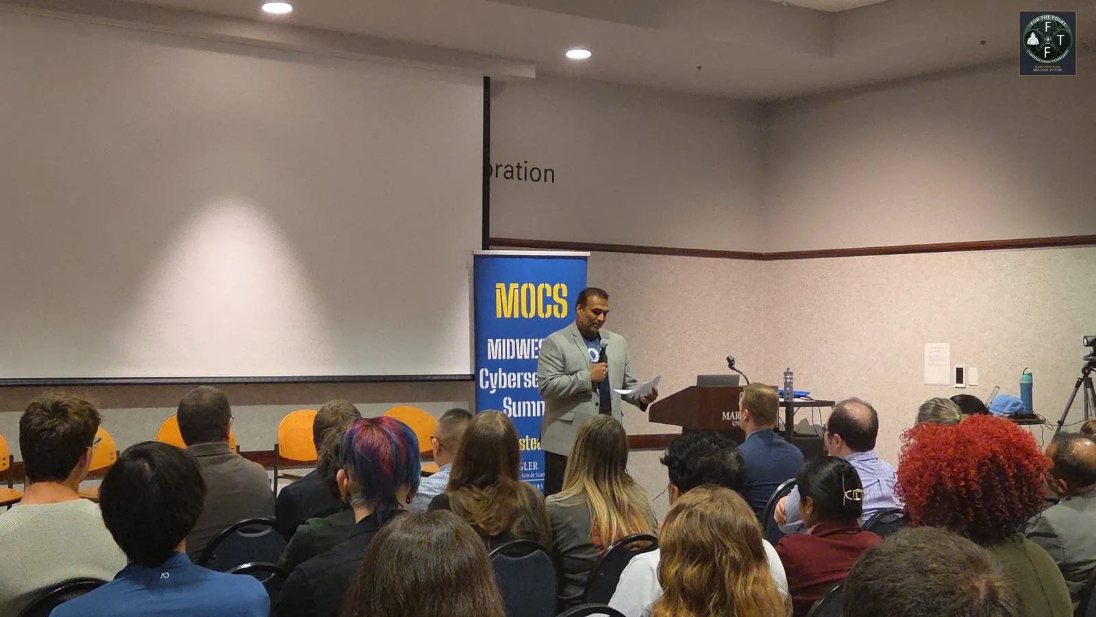 Opening remarks at the podium with MOCS banner